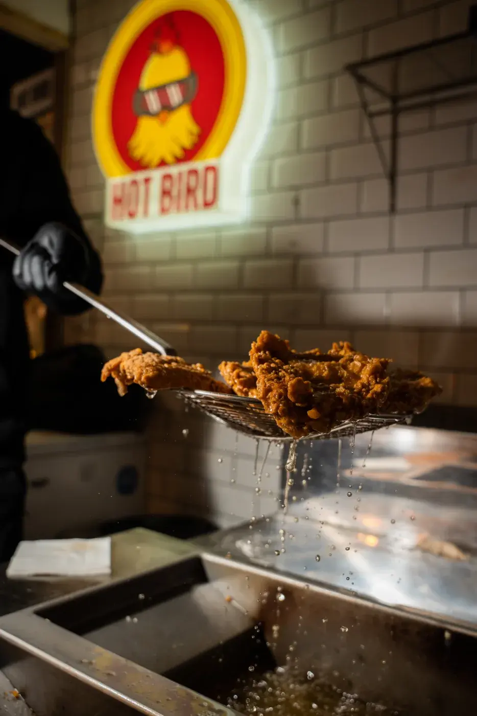 Crispy chicken lifted from the fryer under the neon sign